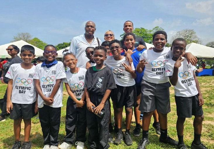 INSPIRING THE NEXT GENERATION: Trinidad and Tobago’s first Olympic gold medallist Hasely Crawford (left, back row), TTOC president Diane Henderson and Kanoo’s Zwede Hewitt pose with a group of children at the TTOC Olympic Day display of sports at the Queen’s Park Savannah, in Port of Spain, on Friday. Kanoo sponsored 300 Olympic Day jerseys for children. (Image obtained at trinidadexpress.com)